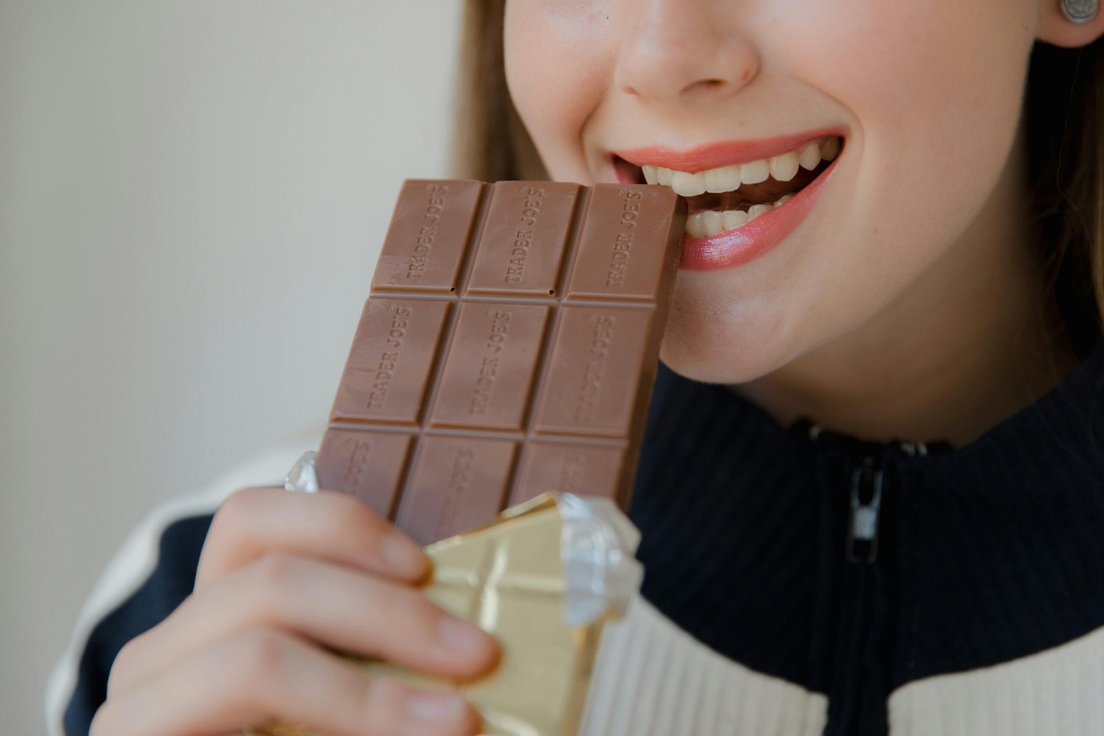 Can braces fix bite problems? Close-up shot of a smiling woman biting into a chocolate bar indoors.